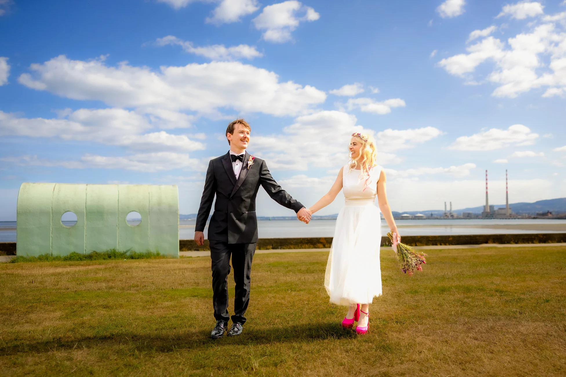 Bride and groom walking naturally together beneath a bright blue Irish sky