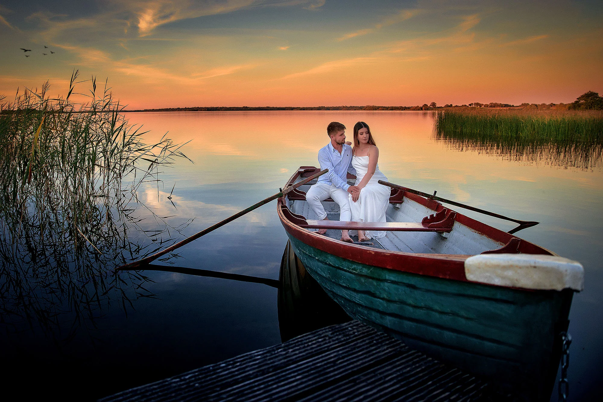 Bride and groom sitting together in a rowing boat at sunset